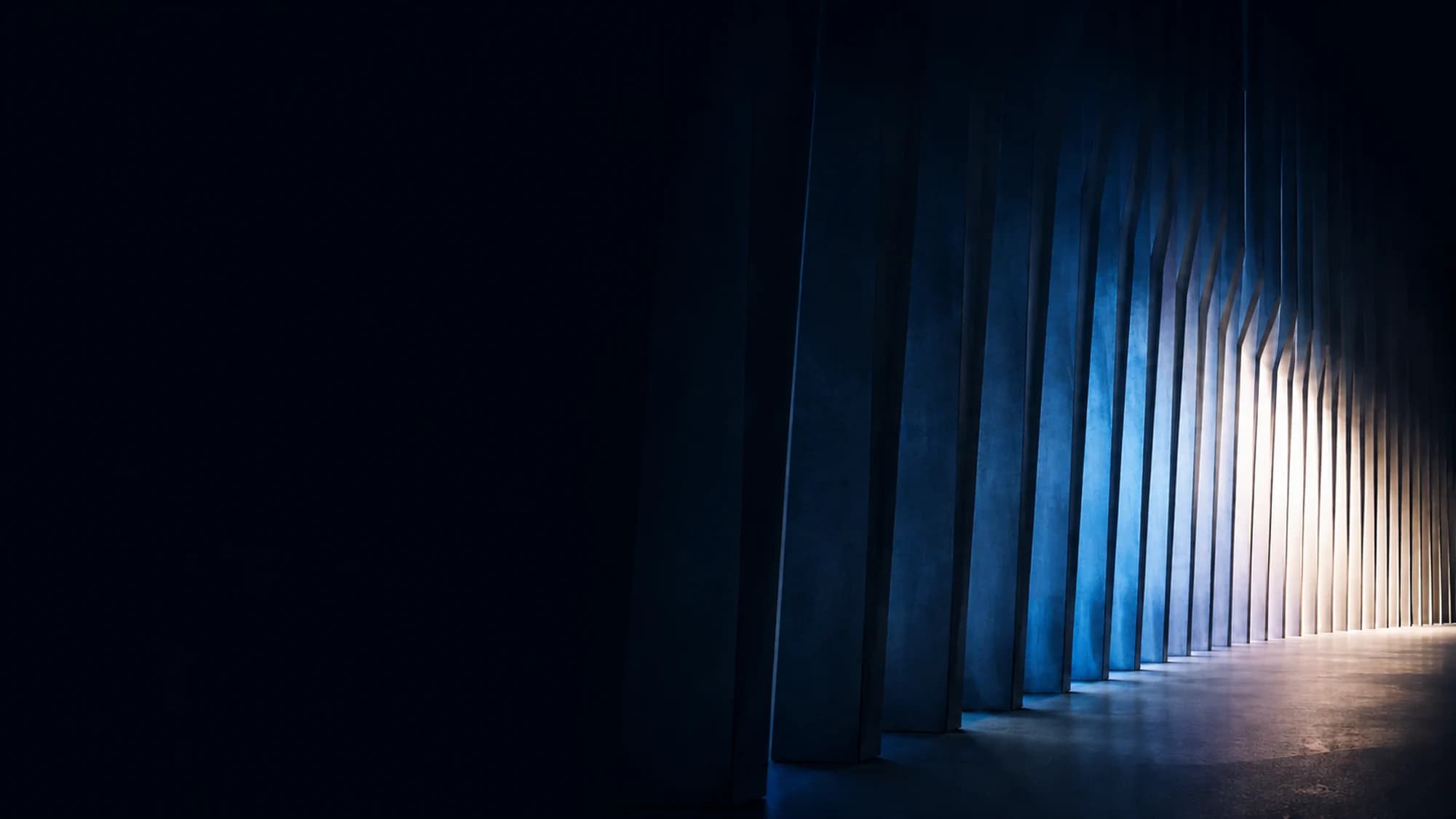Monumental dark corridor with cobalt columns opening into warm light